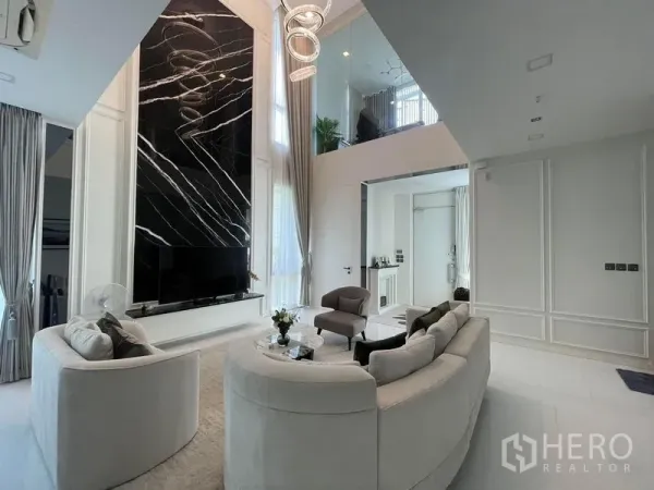 Detached House for rent in Bueng Kum, Bangkok - Double-height living room with black marble feature wall, circular chandelier, curved sofas and tall drapes.