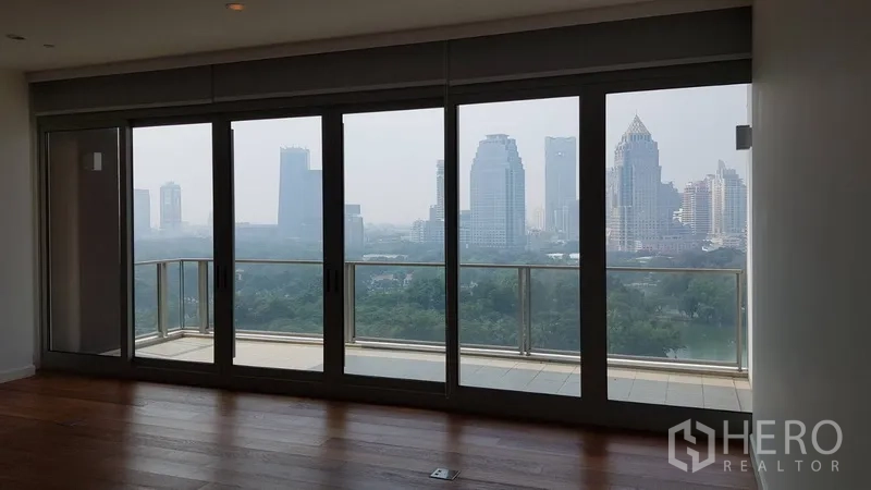 Condominium for rent in Pathum Wan, Bangkok - Living area facing full-height doors to the balcony with a green park outlook.