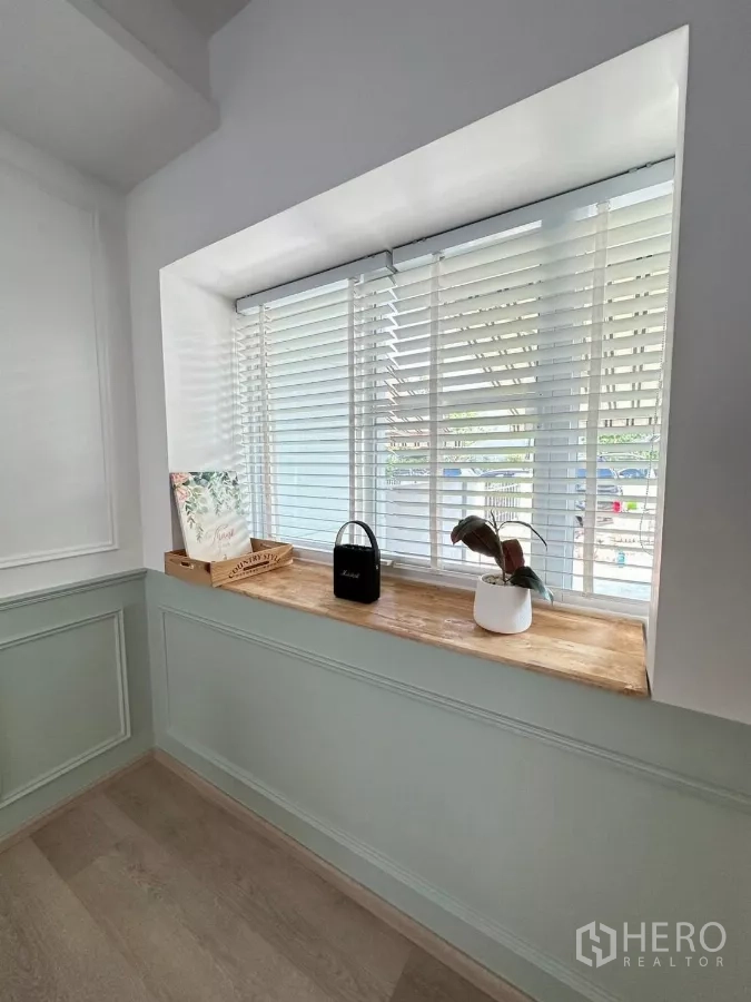 ทาวน์เฮาส์ ให้เช่าในBang Phli, Samut Prakan - มุมหน้าต่างบานกว้างพร้อมมู่ลี่สีขาวและชั้นวางไม้ในห้องนั่งเล่น