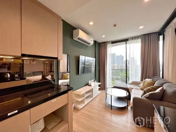Condominium for sale in Watthana, Bangkok - Bright lounge with floor‑to‑ceiling windows, city view from the balcony, and an L‑shaped sofa.