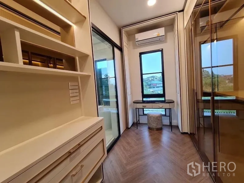 Detached House for rent or sale in Saphan Sung, Bangkok - Walk-in closet with built-in shelving, glass wardrobes and a small vanity desk.