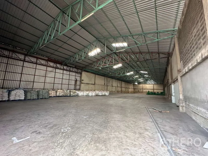 货栈 出租在Mueang Pathum Thani, Pathum Thani - 开阔仓储大厅，混凝土地面、绿色钢梁与侧边装卸区。