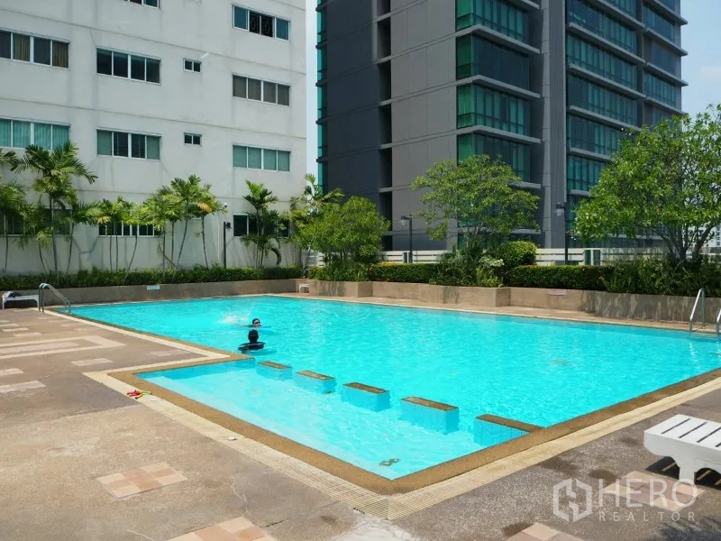 Condominium for rent or sale in Watthana, Bangkok - Outdoor swimming pool with sun deck surrounded by city buildings and greenery.