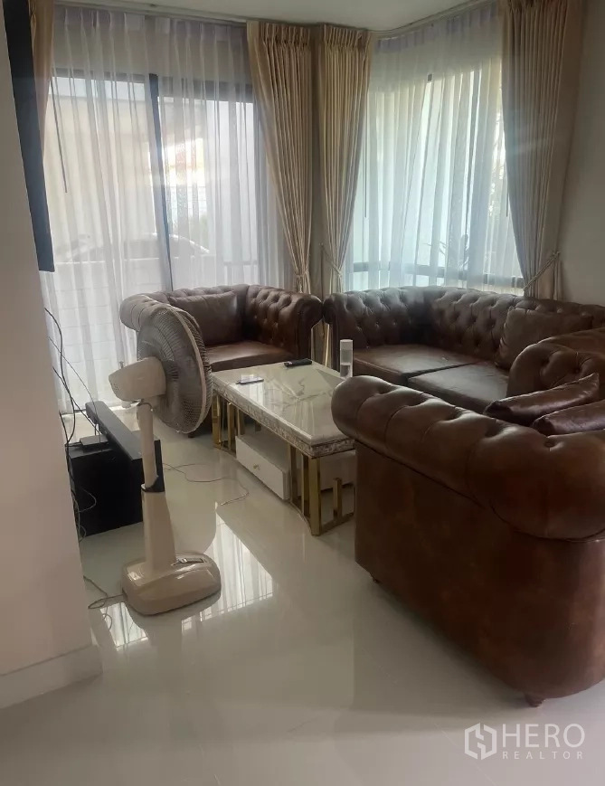 บ้าน ให้เช่าหรือขายในSaphan Sung, Bangkok - มุมห้องนั่งเล่น กระจกบานใหญ่ ม่านโปร่ง โซฟาหนังสีน้ำตาล