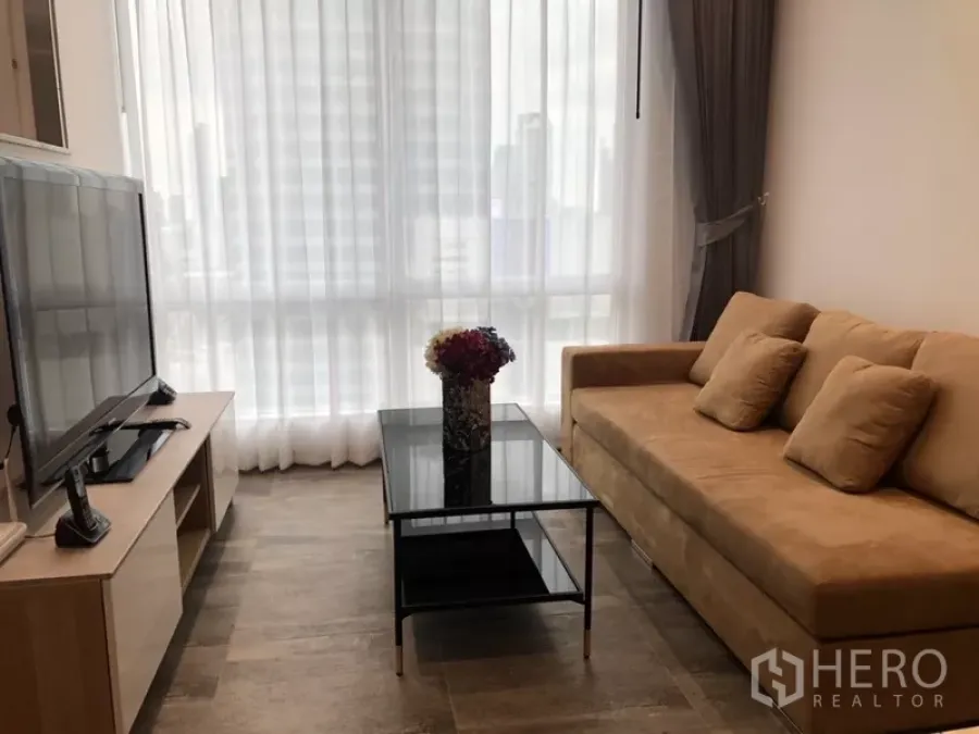 公寓 出租在Sathon, Bangkok - 舒适起居区，米色沙发与黑色玻璃茶几，整面落地窗配纱帘。