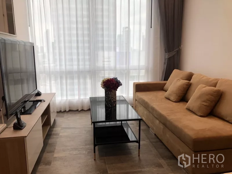 公寓 出租在Sathon, Bangkok - 舒适起居区，米色沙发与黑色玻璃茶几，整面落地窗配纱帘。