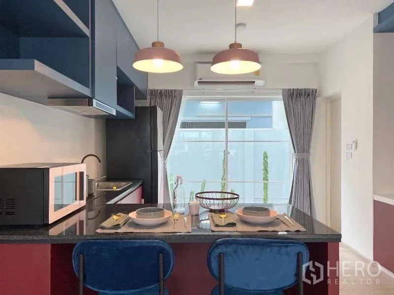 Townhouse for rent in Bang Bo, Samut Prakan - Kitchen with breakfast bar for two, twin pendant lights, refrigerator and glass door bringing natural light.