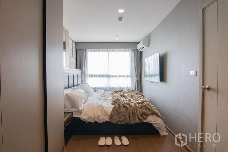Condominium for rent in Phra Khanong, Bangkok - Spacious master bedroom with big window, wall-mounted TV and wooden floor.