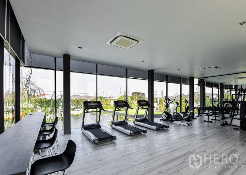 Detached House for rent in Samut Prakan - Fitness center with treadmills and panoramic windows overlooking greenery.