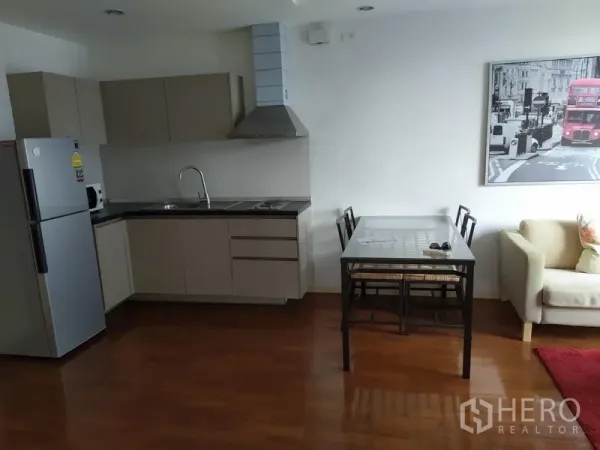 Condominium for sale in Khlong Toei, Bangkok - Modern L-shaped kitchen with cooktop, hood and a dining table beside it.
