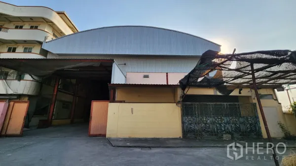 Warehouse for rent in Nonthaburi - Street-facing view of a metal-clad warehouse with wide sliding gates in Bang Bua Thong.