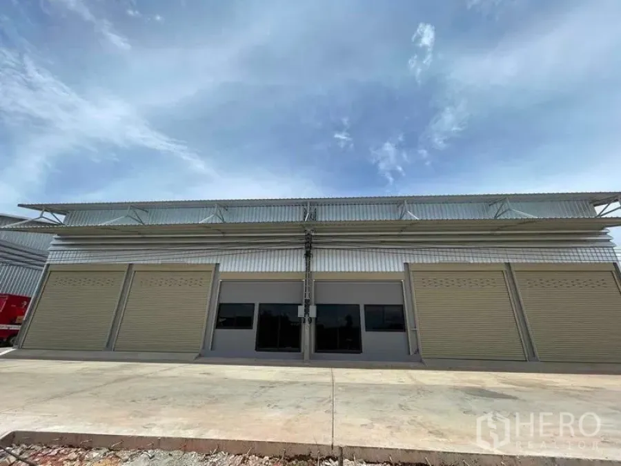 Warehouse for rent in Phra Samut Chedi, Samut Prakan - Front elevation of the warehouse featuring a central glass entry and multiple rolling doors along a concrete apron.