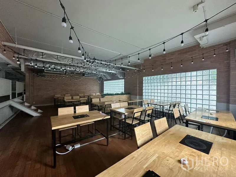 零售空间 出租在Watthana, Bangkok - 楼上用餐区，木桌内置电煮炉与串灯装饰。