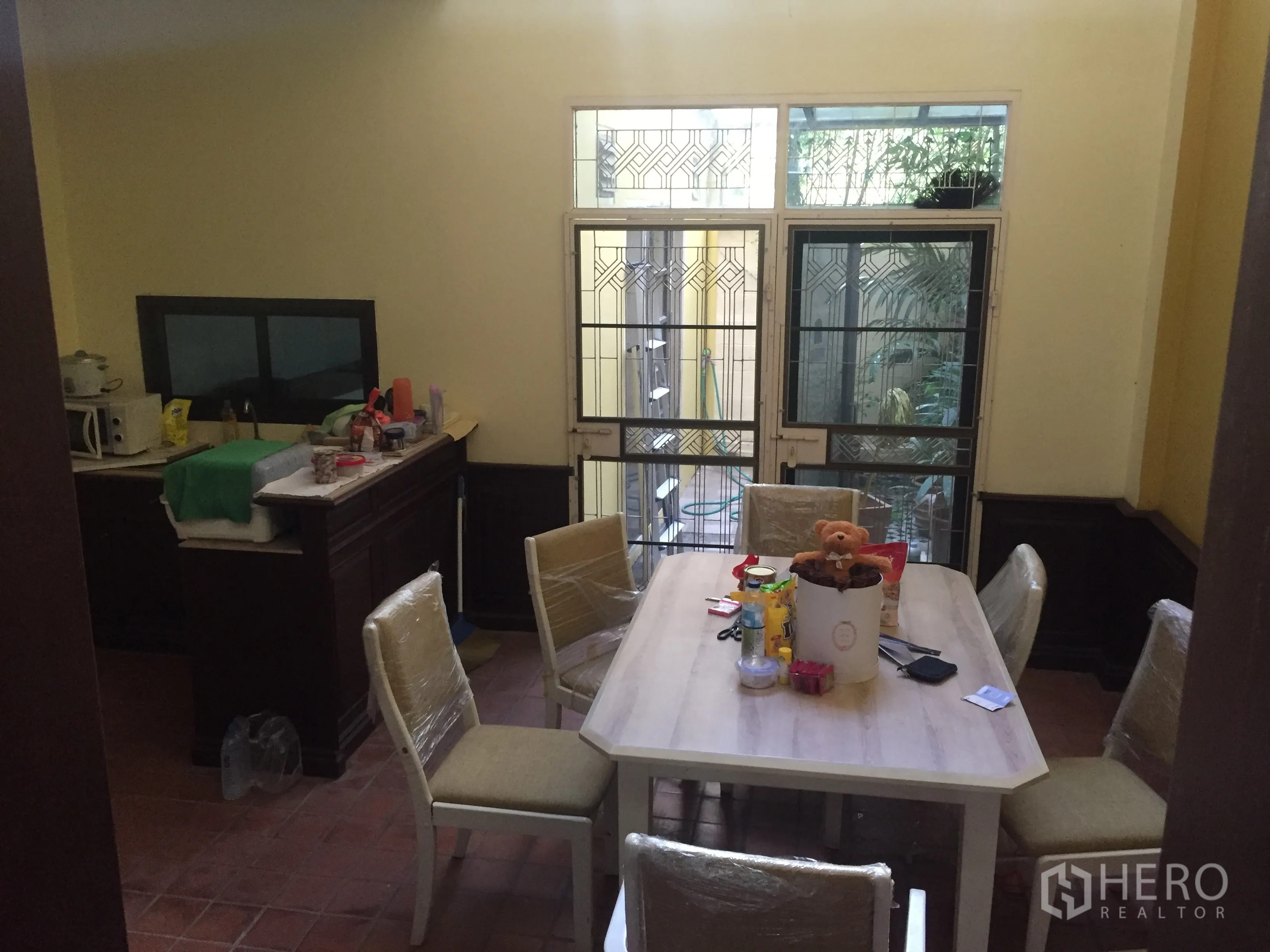 Townhouse for rent in Khlong Toei, Bangkok - Dining space beside a simple kitchen with patio doors and patterned window grilles.