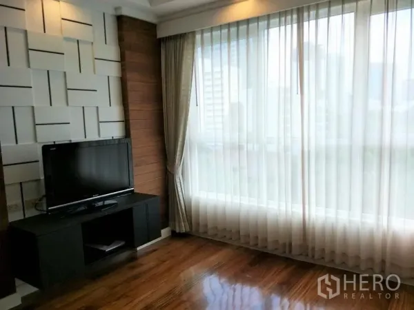 Condominium for rent or sale in Watthana, Bangkok - Sunlit room with floor‑to‑ceiling windows, sheer curtains and a TV on a media console.