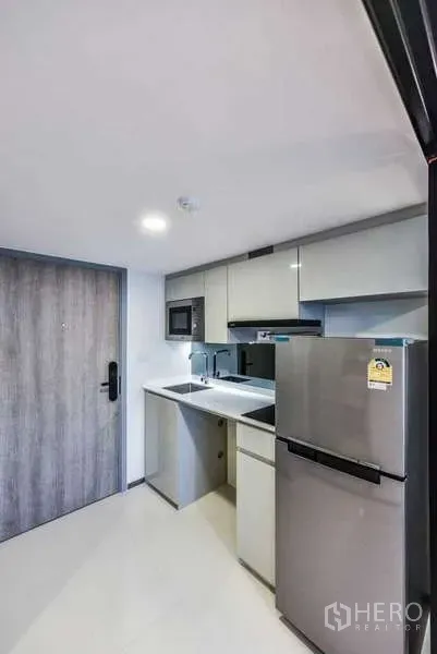 Condominium for rent in Huai Khwang, Bangkok - Compact entry kitchen with glossy cabinets, sink, microwave and stainless refrigerator.