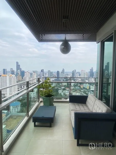 公寓 出租在Watthana, Bangkok - 狭长阳台，户外沙发、玻璃护栏与宽阔城市景观。