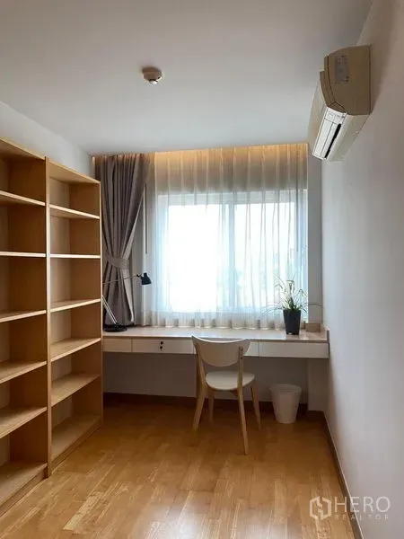 Condominium for sale in Phra Khanong, Bangkok - Small study room with wall-mounted desk, open shelving, wood flooring, and window light.