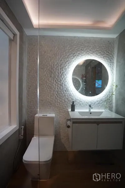 Townhouse for rent in Khlong Toei, Bangkok - Contemporary bathroom with a backlit round mirror, textured feature wall and floating vanity.