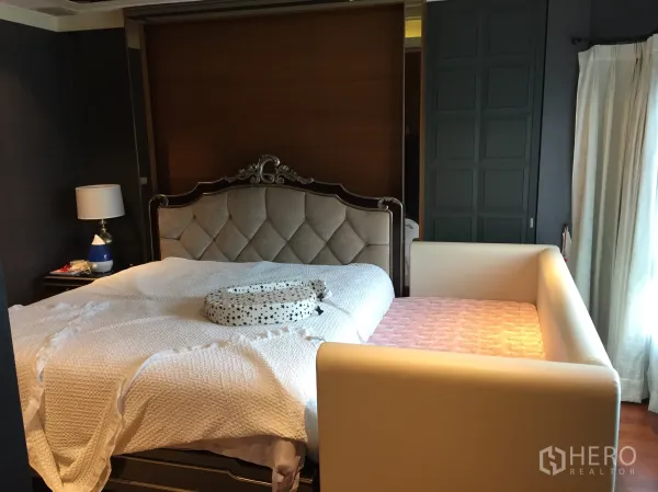 Detached House for sale in Saphan Sung, Bangkok - Primary bedroom with tufted headboard, bedside table and a baby daybed beside the window.