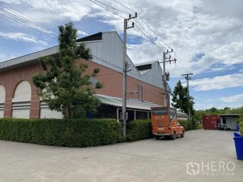 货栈 出租在Samut Sakhon - 仓库建筑转角，绿篱和后勤区域。