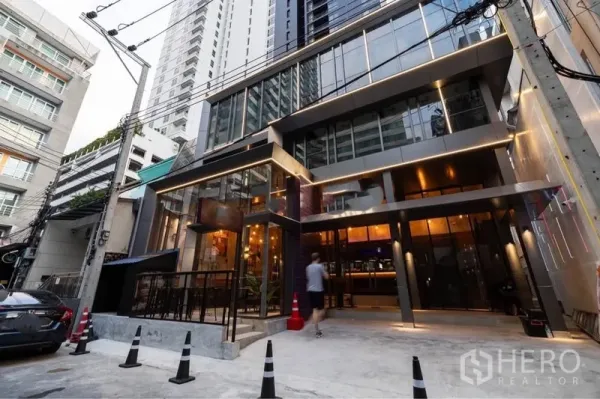 零售空间 出租在Watthana, Bangkok - 现代玻璃立面商业楼外观，灯光温暖，临街出入口位于繁华小巷。