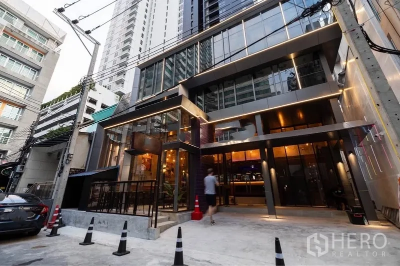 零售空间 出租在Watthana, Bangkok - 现代玻璃立面商业楼外观，灯光温暖，临街出入口位于繁华小巷。