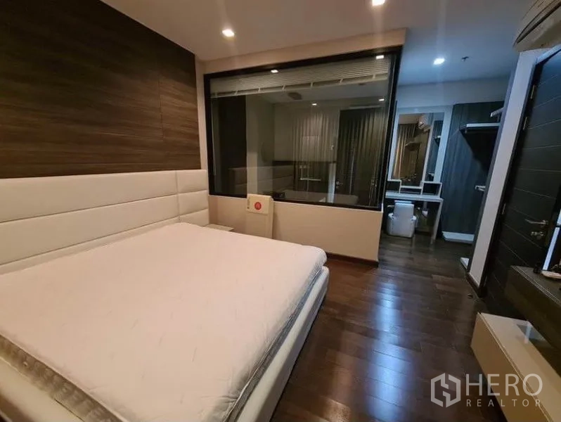 Condominium for rent or sale in Huai Khwang, Bangkok - Master suite with glass-partitioned ensuite bathroom and warm wood flooring.