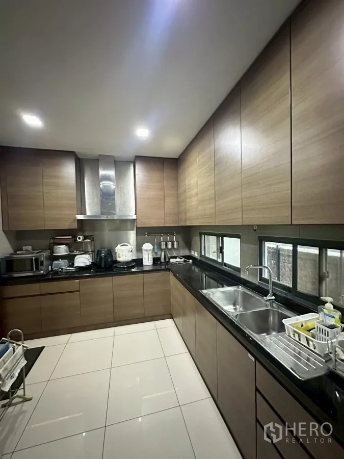Detached House for sale in Bang Lamung, Chon Buri - Fully fitted kitchen with wood cabinets, black countertops and double sink.