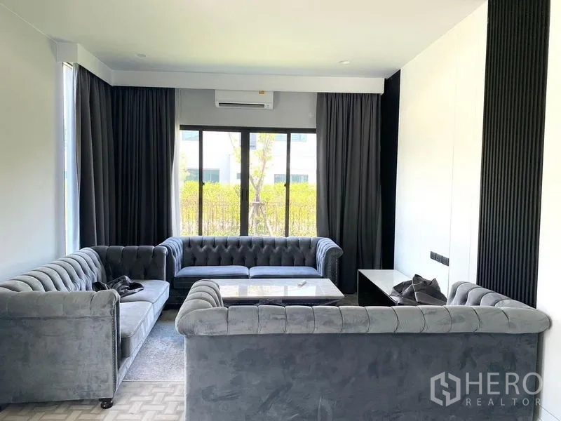 Detached House for sale in Bang Kapi, Bangkok - Cozy living room featuring grey tufted sofas, coffee table and wide sliding windows.