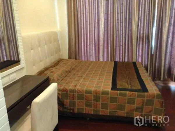 Condominium for rent or sale in Watthana, Bangkok - Warm 1-bedroom with upholstered headboard, vanity desk and floor-to-ceiling curtains over wood flooring.