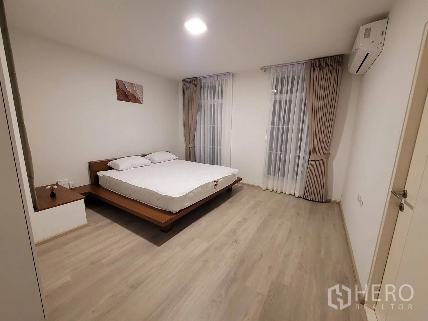 联排别墅 出租在Prawet, Bangkok - 宽敞主卧，平台床、空调与落地窗帘。