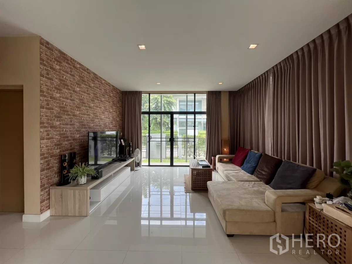 Detached House for rent in Bang Kapi, Bangkok - Bright living room with brick accent wall, sectional sofa, and large windows.