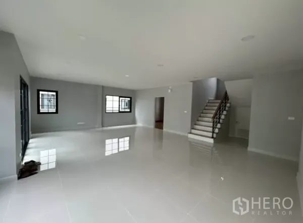 独立式住宅 出租在Bang Phli, Samut Prakan - 客厅另一角度，楼梯与多扇窗户，墙面为灰色基调。