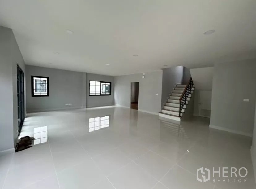 独立式住宅 出租在Bang Phli, Samut Prakan - 客厅另一角度，楼梯与多扇窗户，墙面为灰色基调。