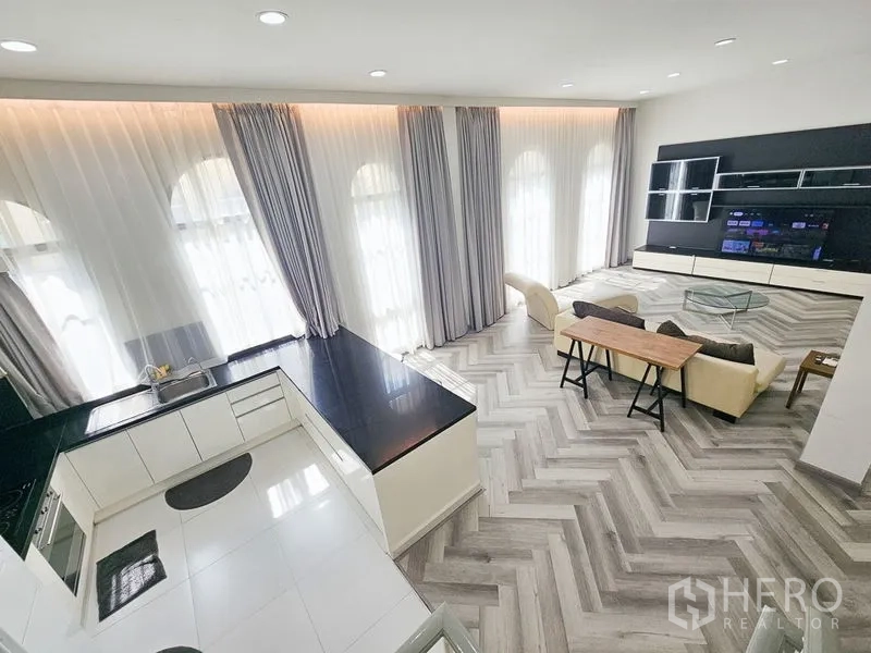 Townhouse for rent in Yan Nawa, Bangkok - Open-plan living with herringbone floors, tall arched windows, a white U-shaped kitchen and a built-in media wall.