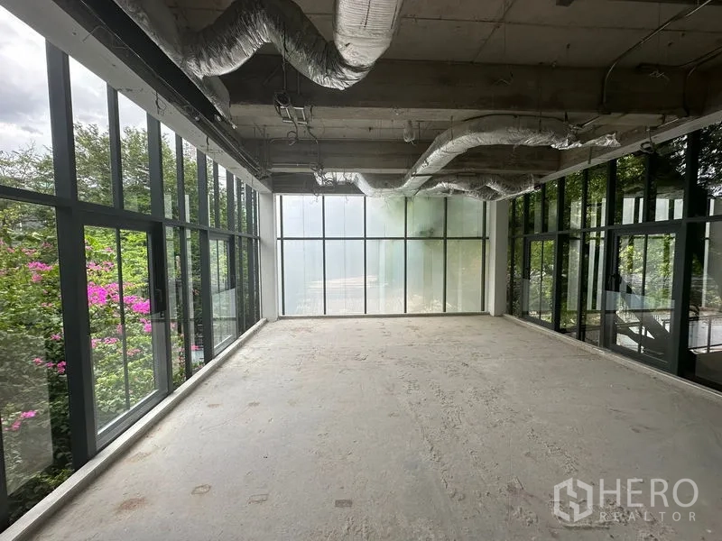 Office Space for rent in Khlong Toei, Bangkok - Shell-and-core office with floor-to-ceiling glass walls and exposed ducts overlooking greenery.