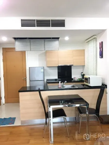 Condominium for rent in Watthana, Bangkok - Compact kitchen with black countertops, light wood cabinets and a dining set.