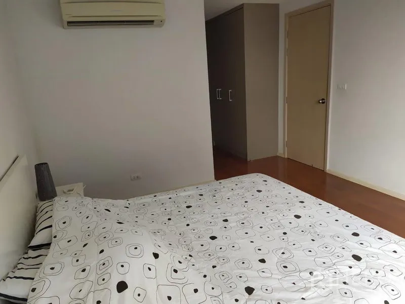 Condominium for sale in Khlong Toei, Bangkok - Cozy bedroom with patterned bedding, air conditioning unit and wardrobe.