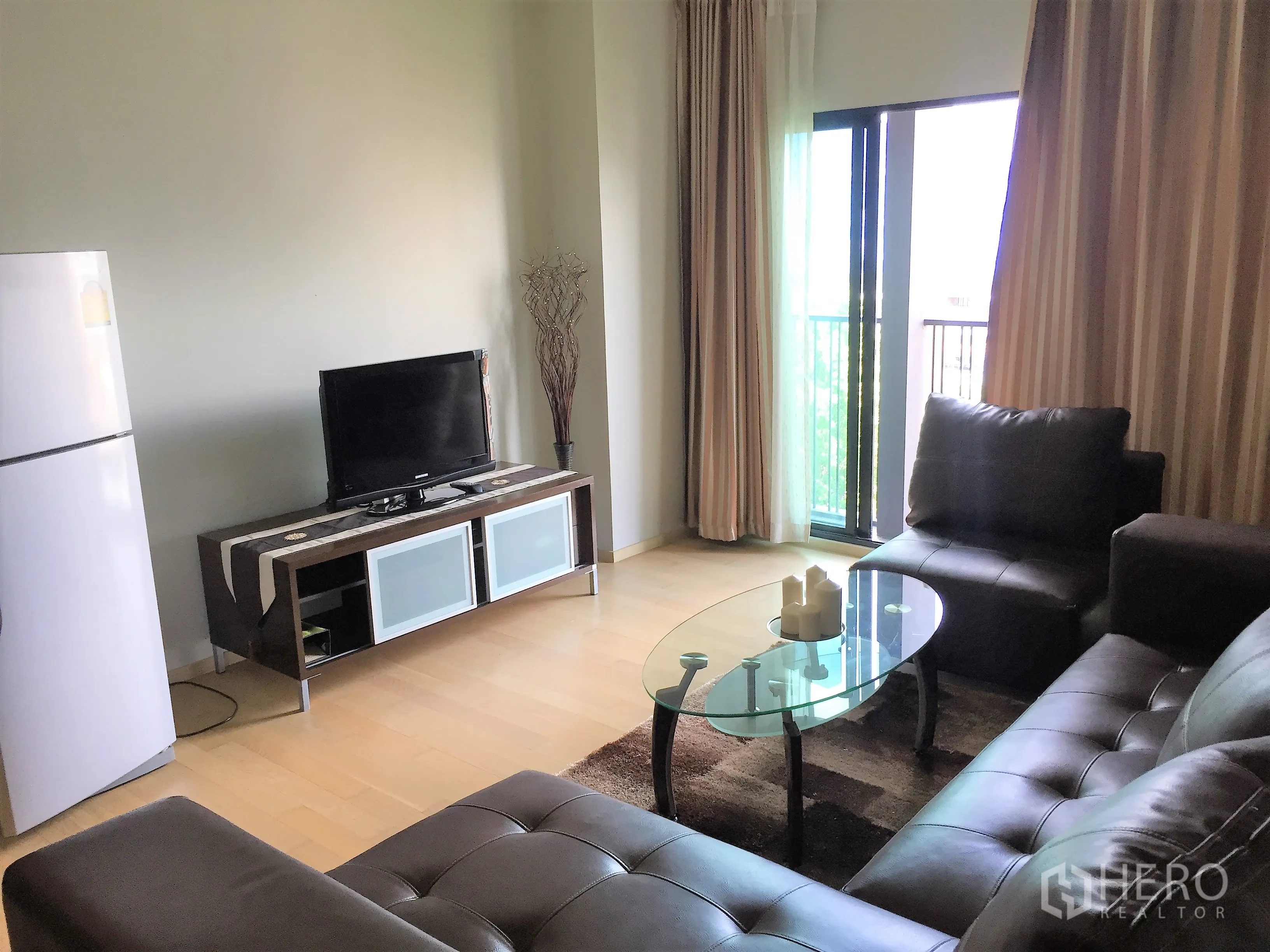 Condominium for rent in Watthana, Bangkok - Bright living room with TV console, glass coffee table, leather seating, and balcony access.