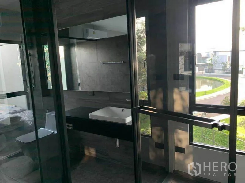 Townhouse for rent in Bang Phli, Samut Prakan - Contemporary bathroom with glass shower, vanity, and views over a landscaped pond.