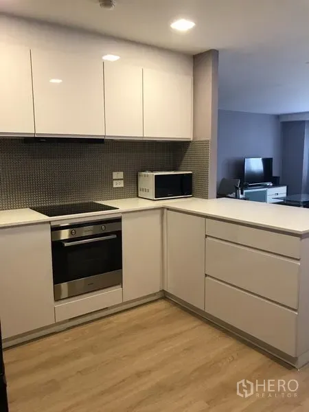 公寓 出租在Bang Rak, Bangkok - U形厨房，亮面橱柜，内置烤箱与电炉，配微波炉，面向客厅。