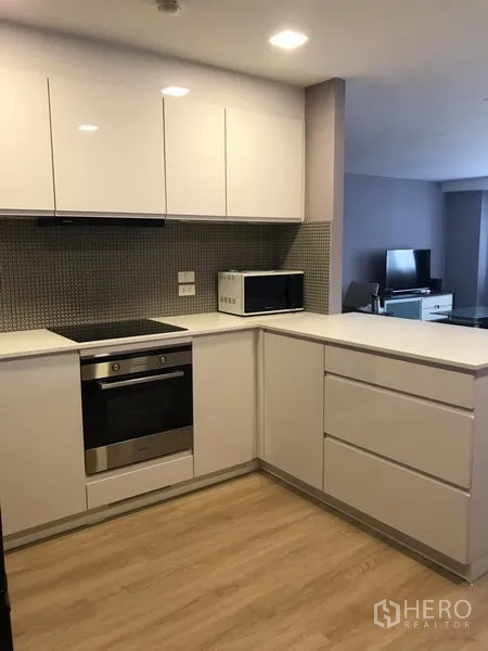 公寓 出租在Bang Rak, Bangkok - U形厨房，亮面橱柜，内置烤箱与电炉，配微波炉，面向客厅。