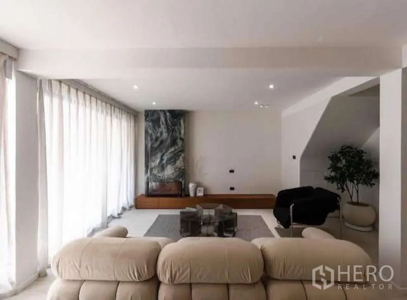 Townhouse for sale in Sathon, Bangkok - Sunlit living room with floor-to-ceiling curtains and stone feature wall.