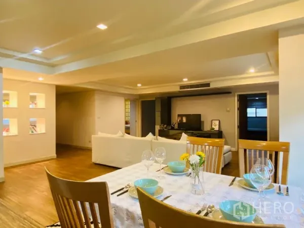 Condominium for rent in Watthana, Bangkok - Dining area set for four with wooden chairs and table, overlooking the lounge and TV unit.