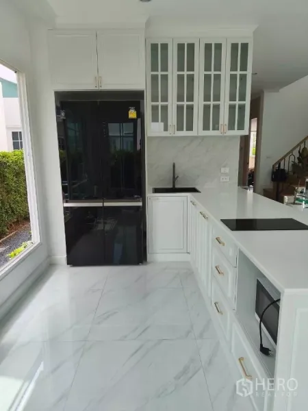 Detached House for rent in Bang Phli, Samut Prakan - Kitchen angle showing black double-door fridge, induction cooktop, oven, and marble-look floors.
