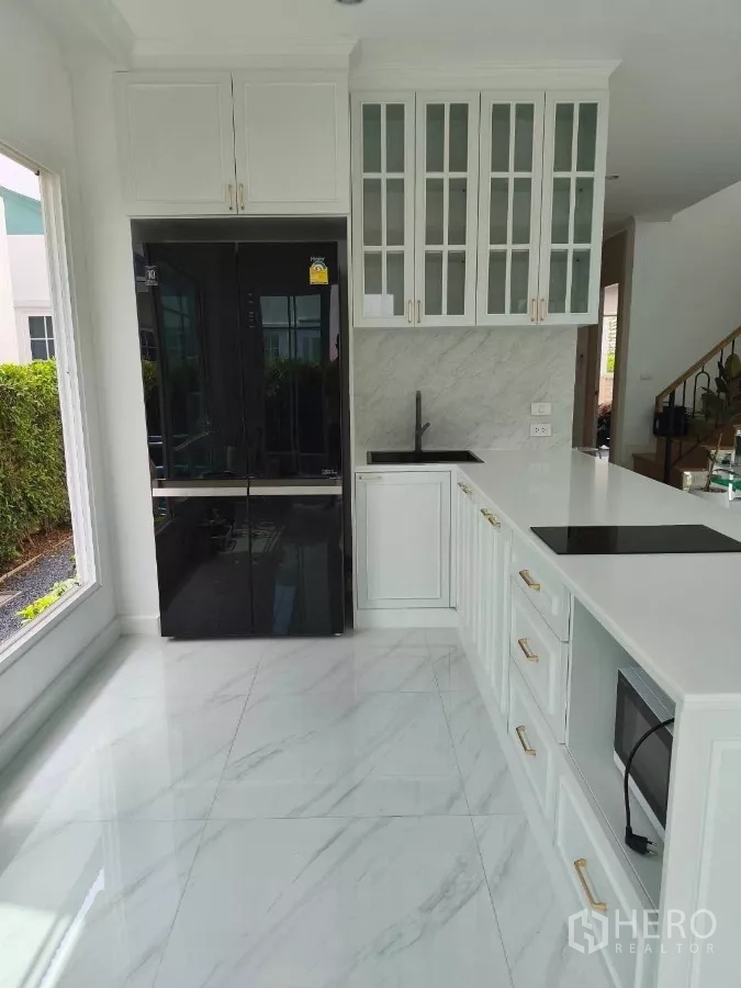 Detached House for rent in Bang Phli, Samut Prakan - Kitchen angle showing black double-door fridge, induction cooktop, oven, and marble-look floors.