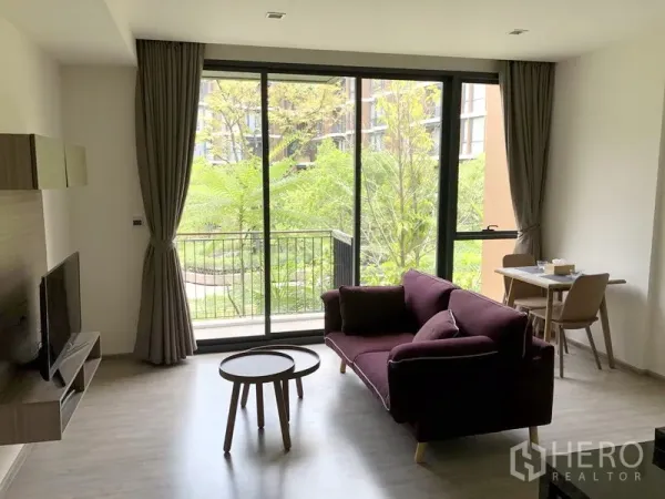 คอนโด ให้เช่าในWatthana, Bangkok - ห้องนั่งเล่นสว่างโปร่ง ผนังกระจกสูงจรดเพดาน พร้อมระเบียงและวิวสวนเขียวที่มอริ เฮาส์