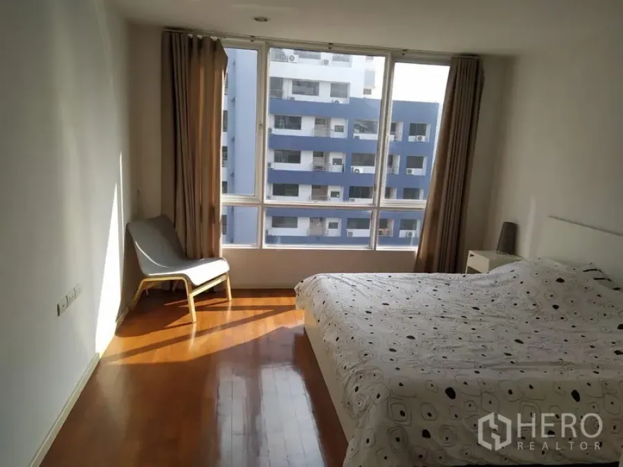 Condominium for sale in Khlong Toei, Bangkok - Large bedroom with floor-to-ceiling windows, city view and lounge chair.