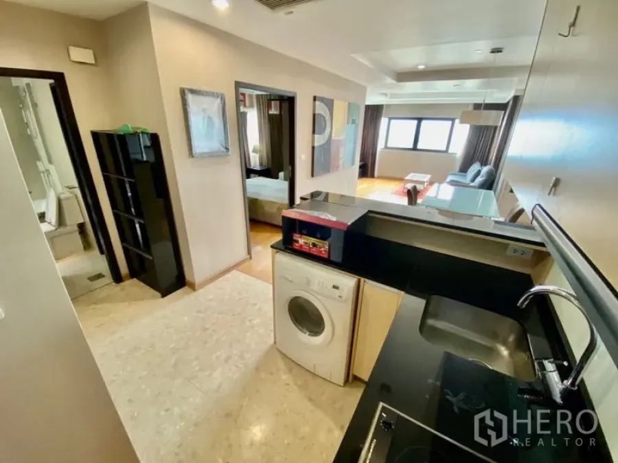 คอนโด ให้เช่าหรือขายในSathon, Bangkok - ครัวบิลท์อินเคาน์เตอร์สีดำพร้อมเครื่องซักผ้า เปิดเชื่อมกับห้องนั่งเล่นและทางเข้าห้องนอน